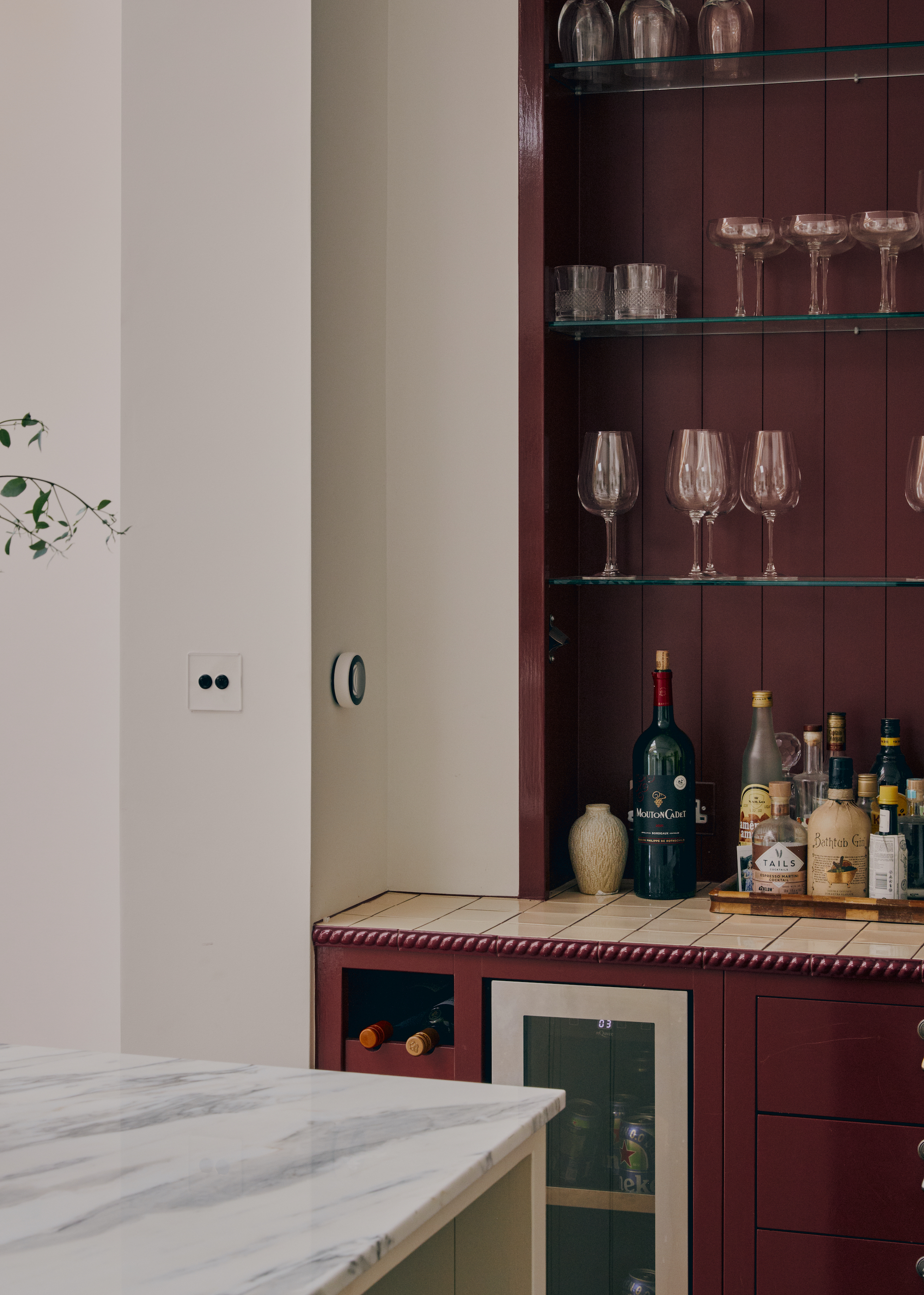 kitchen in deep burgundy with marble tops and a view of glass open shelving with glassware on top including wine glasses