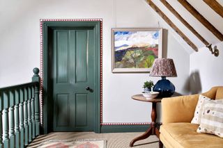A hallway with a green door bordered with a red patterned wallpaper border