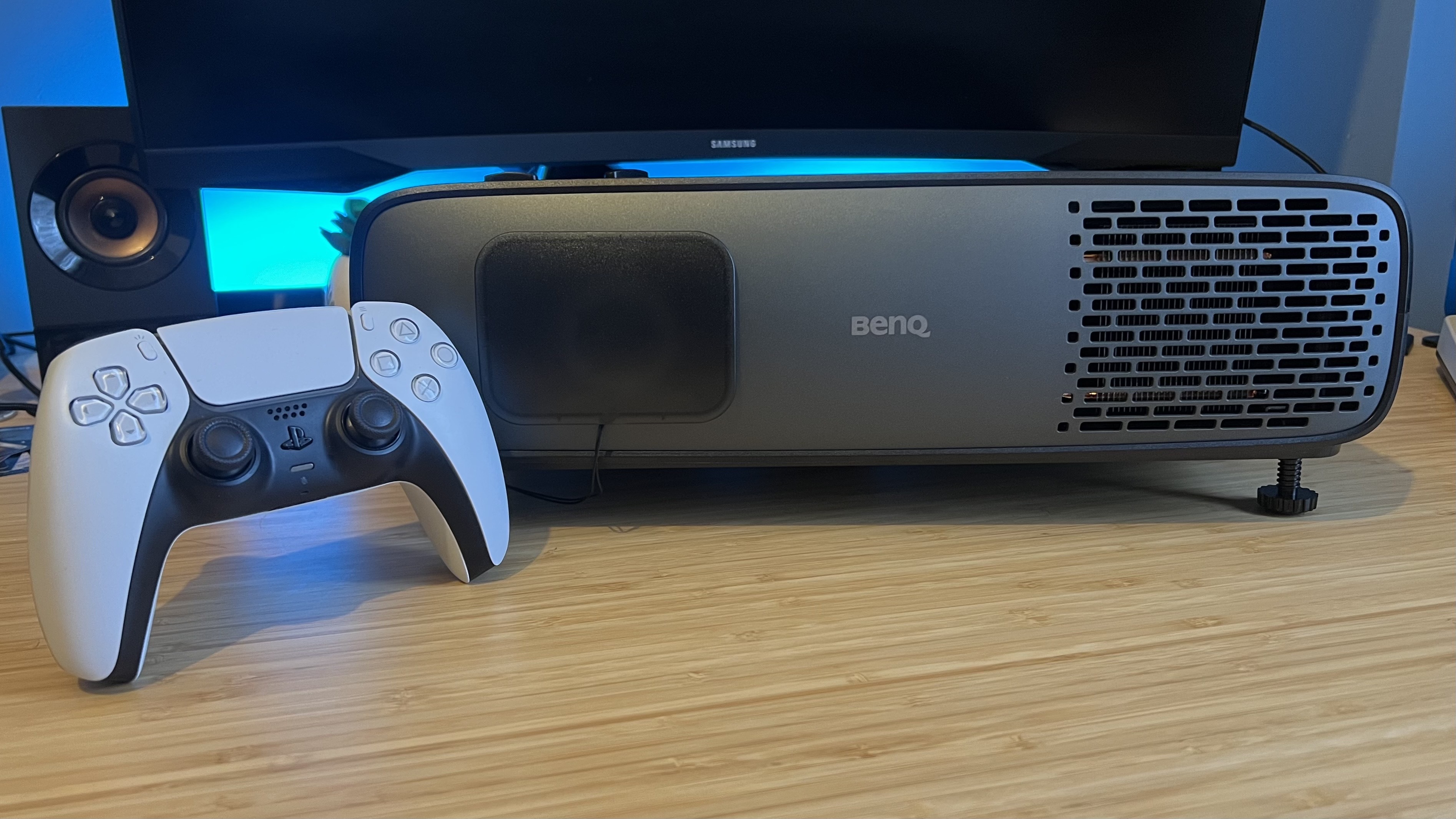 BenQ W4100i projector on a wooden desk with a PS5 DualSense controller