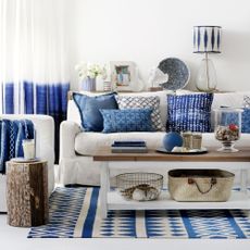 coastal living room with white walls and sofa layered with blue cushions and decor pieces