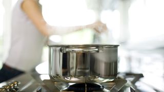 a clean stainless steel pan on the hob with a woman in the background