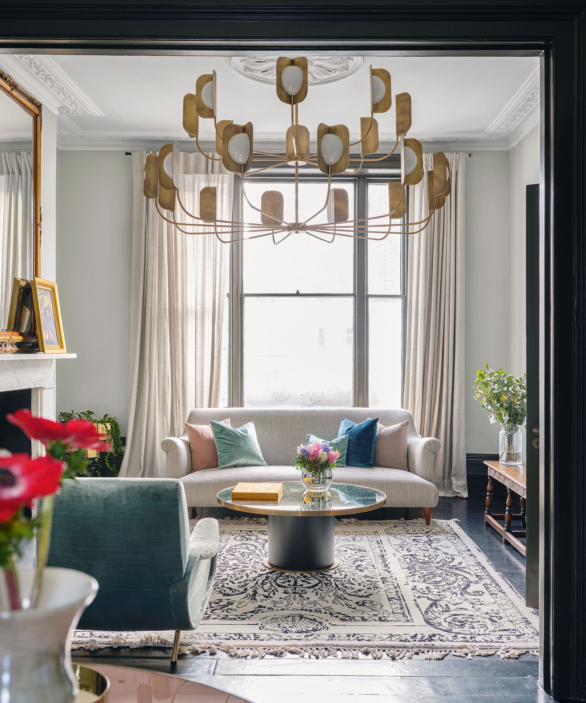 A neutral living room with modern sofa, large window, Persian rug and large gold statement ceiling light.
