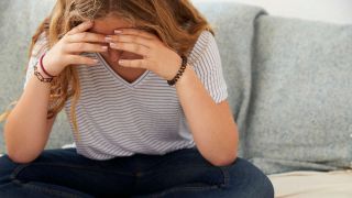 Depressed teenage girl sitting alone at home, head in hands