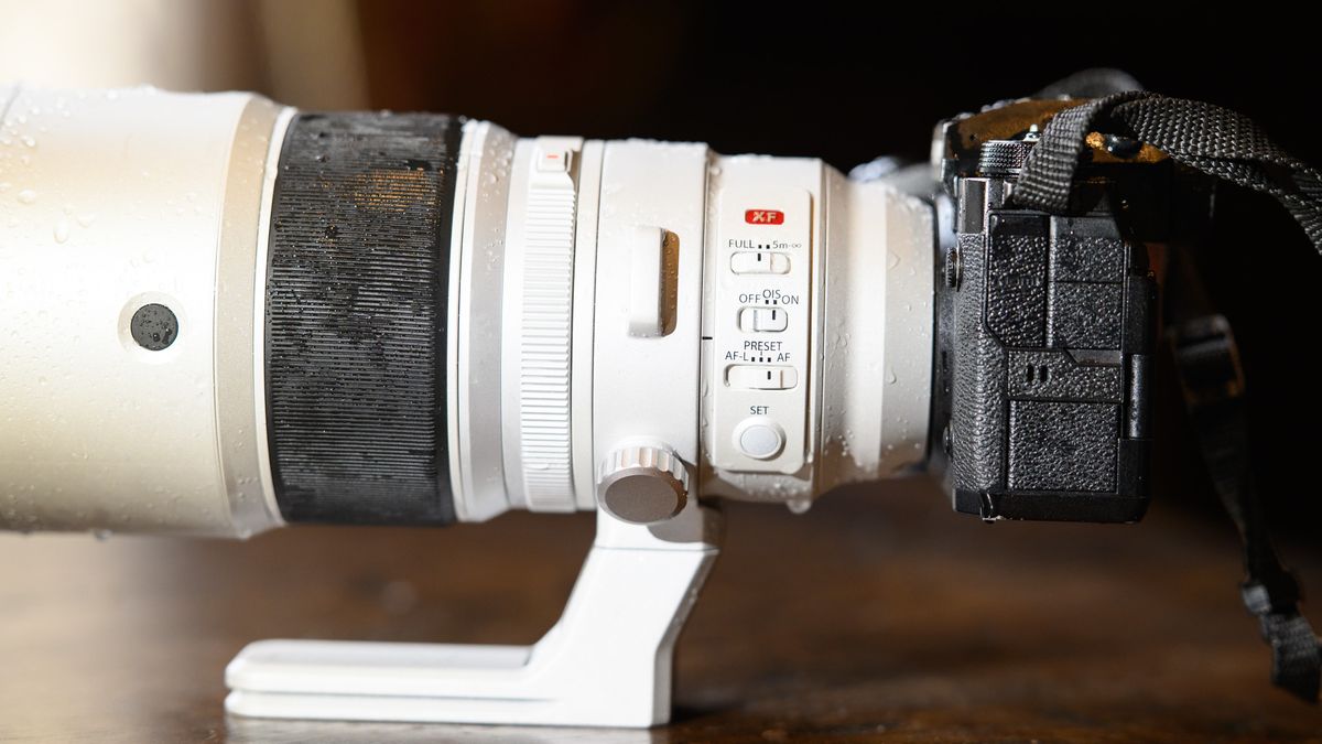 The Fujifilm XF 400mm F4.5 R LM OIS WR telephoto prime lens attached to a Fujifilm X-H2S camera, on a wooden table — close up of the lens controls