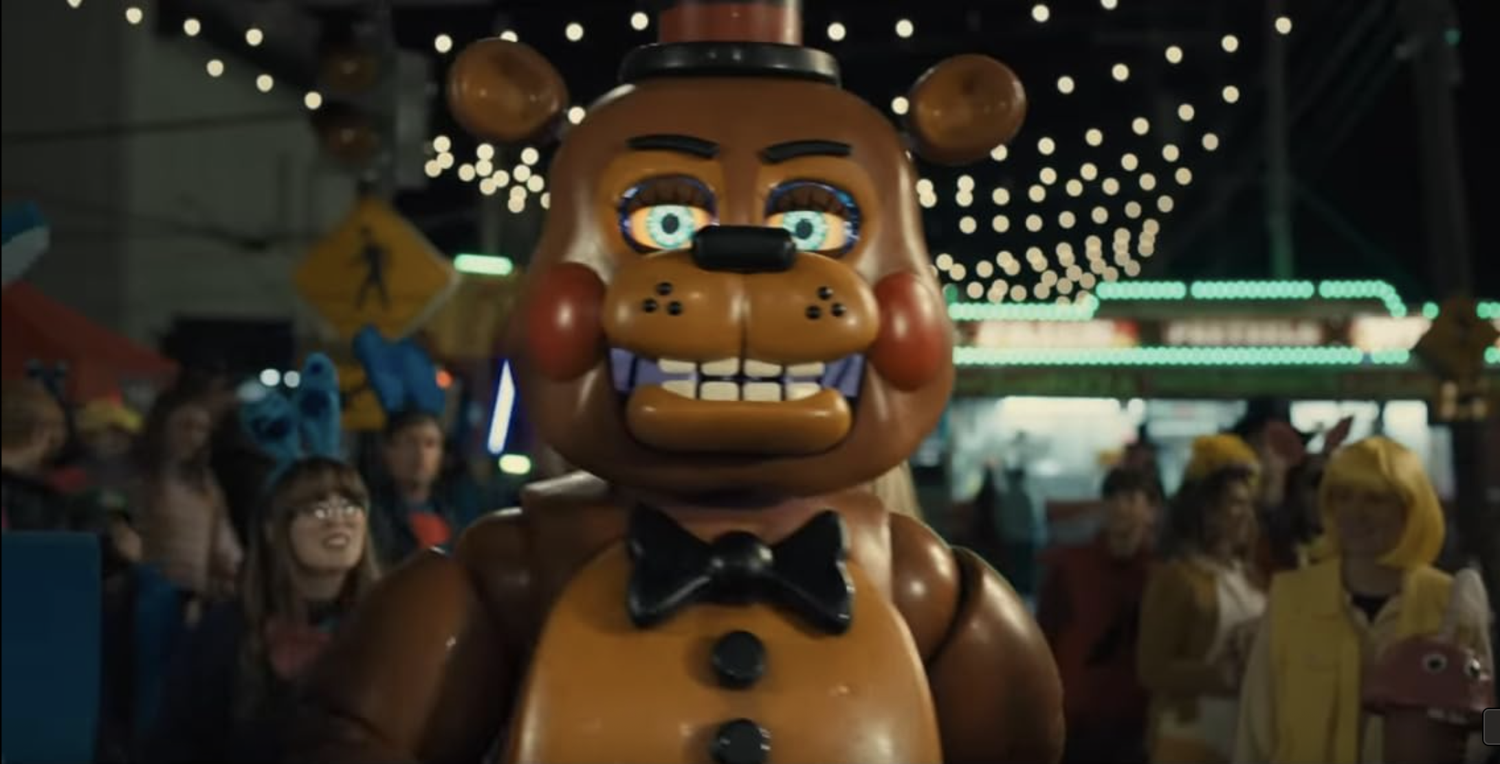 Freddy Fazbear standing in front of a crowd. He is an animatronic teddy bear with glowing blue eyes and a sinister look on his face.