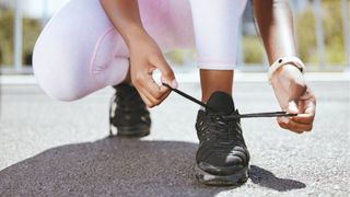 black woman legs arms showing tying shoe lace black shoes on concrete sunny day