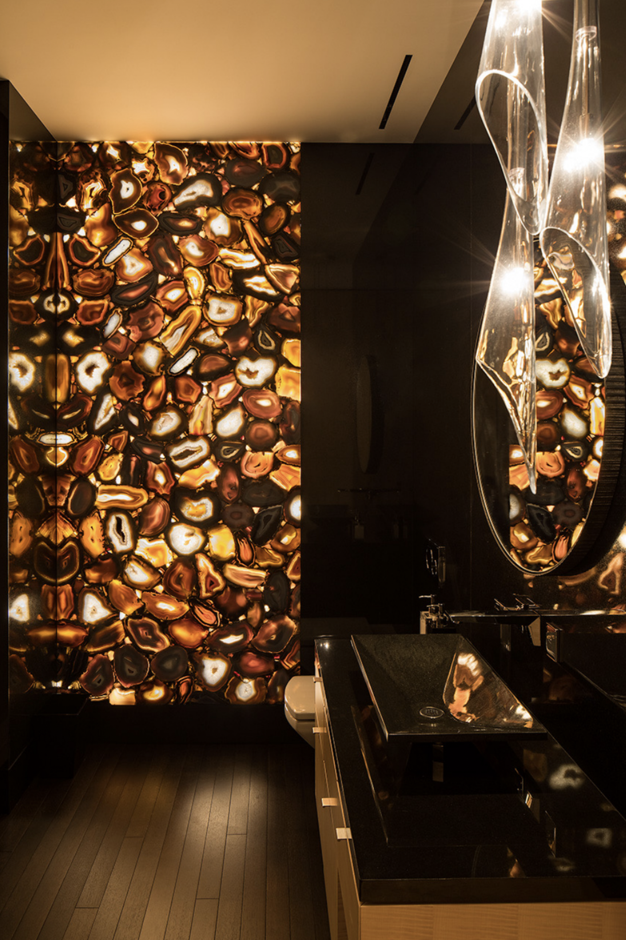 backlit shower wall with onyx-like stone, with black vanity, timber-look flooring,and white ceiling