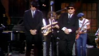 Dan Aykroyd and John Belushi stand dressed as the Blues Brothers during a performance of "Soul Man" on Saturday Night Live.