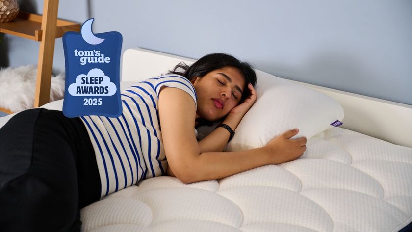 The image shows a dark haired woman sleeping on her side on a white pillow in a blue bedroom. There&#039;s a blue Tom&#039;s Guide Sleep Awards 2025 badge over the top of the image.