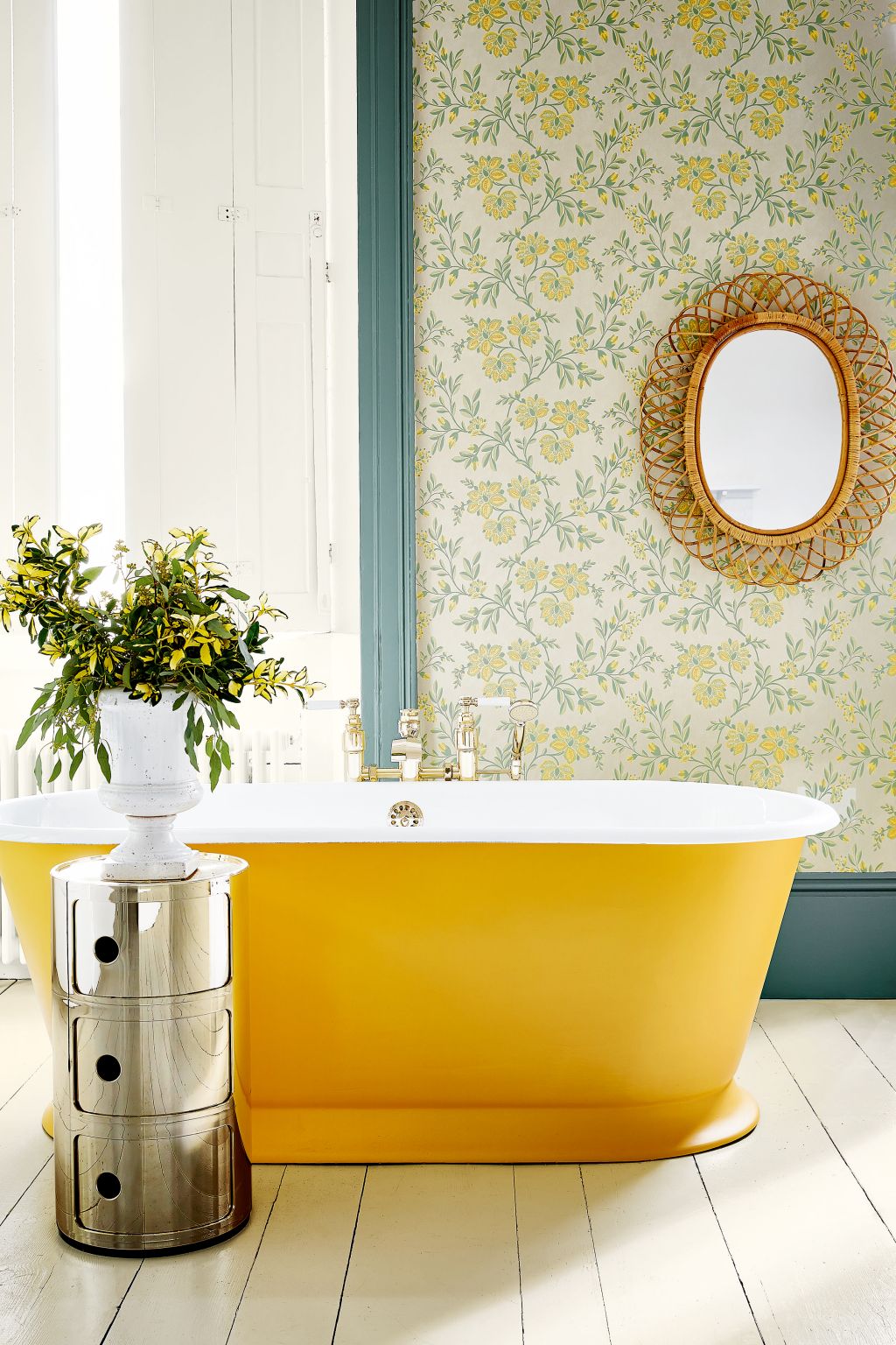 Vintage yellow and green printed wallpaper behind yellow painted roll top bathtub