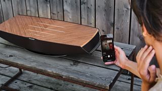 Sonus faber Omnia on a bench outside with a lady controlling music streaming via a phone