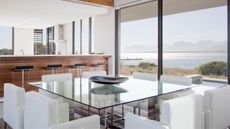 Clean glass dining table with bowl in centre, reflecting light from outside, entering through floor-to-ceiling glass doors overlooking ocean - for article on how to clean a glass table