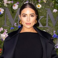 Olivia Culpo wears a black dress, black coat, and has her hair slicked back