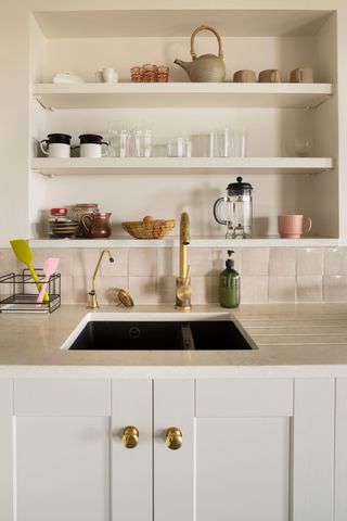 kitchen sink with brass taps white drainer and white tiles and open shelves above