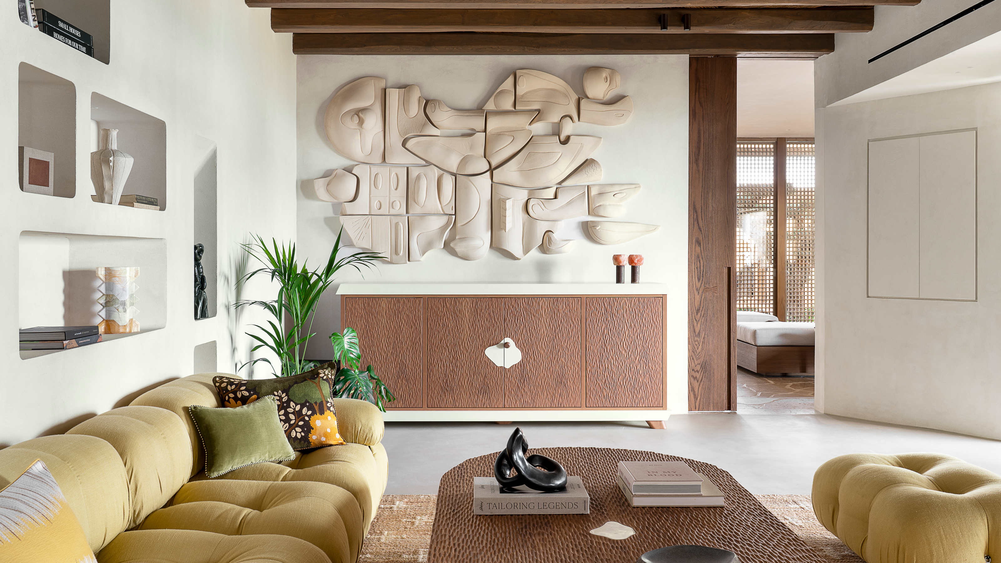 Living room with white walls, textured wood sideboard and coffee table, sculptural wall hanging, yellow sofa