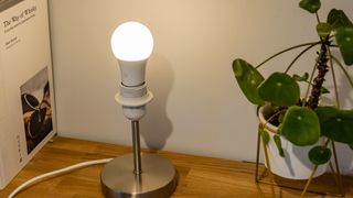 The Hive Smart Light Bulb illuminate white in a lamp on a shelf