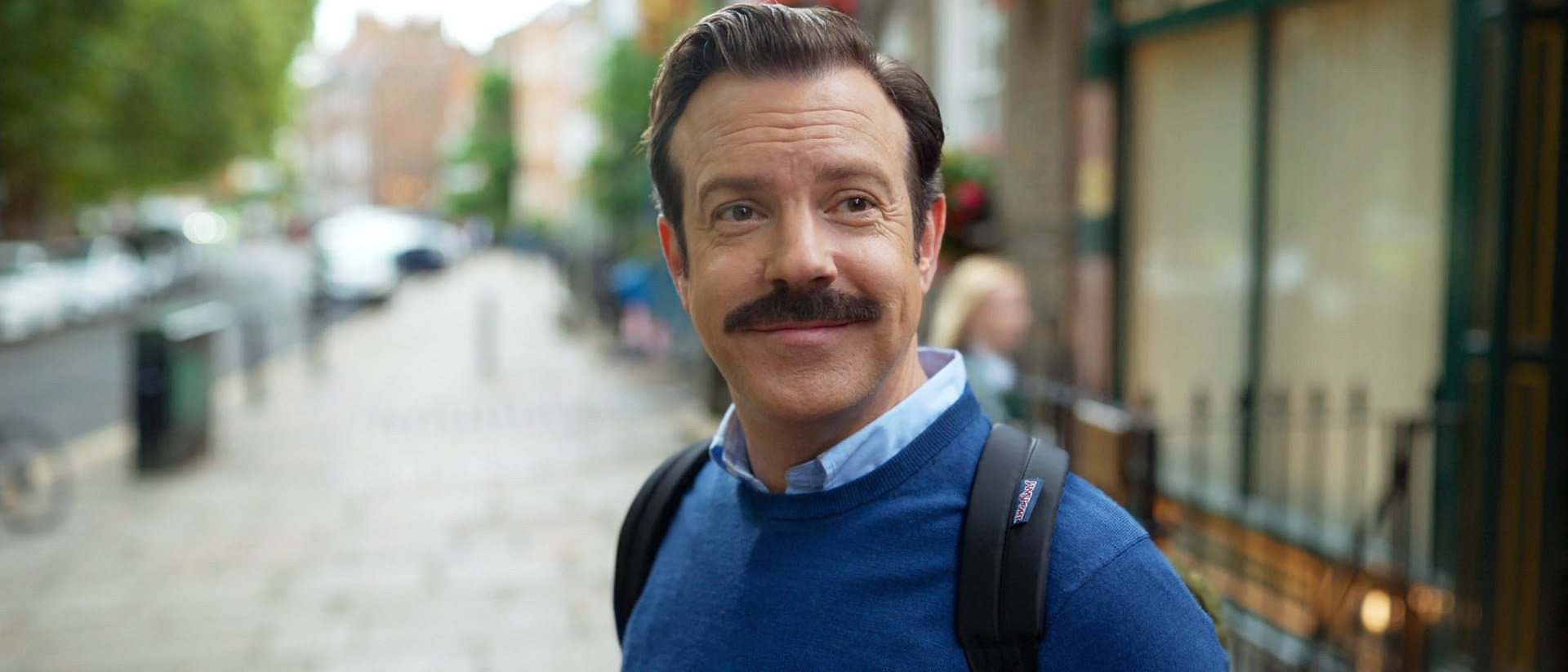 A close-up of Ted smiling as he stands on a street in Ted Lasso season 4 episode 2