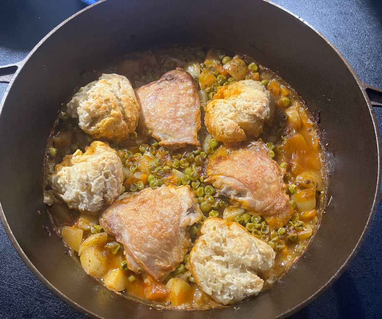 A small bronze colored cast-iron Dutch Oven with a chicken casserole with dumplings inside.