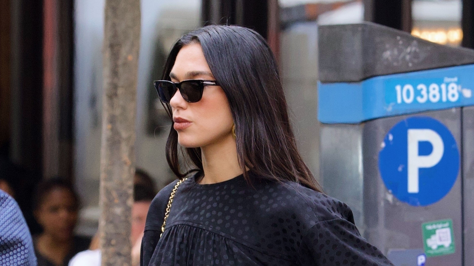 Dua Lipa wearing a black top, black jeans, and black sunglasses