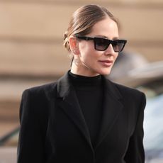 woman with glossy hair and glowy skin in sunglasses and a black blazer and roll neck