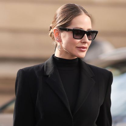 woman with glossy hair and glowy skin in sunglasses and a black blazer and roll neck
