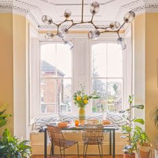 Glass and brass sputnik style light near bay window in yellow room, above table and chairs in a dining nook