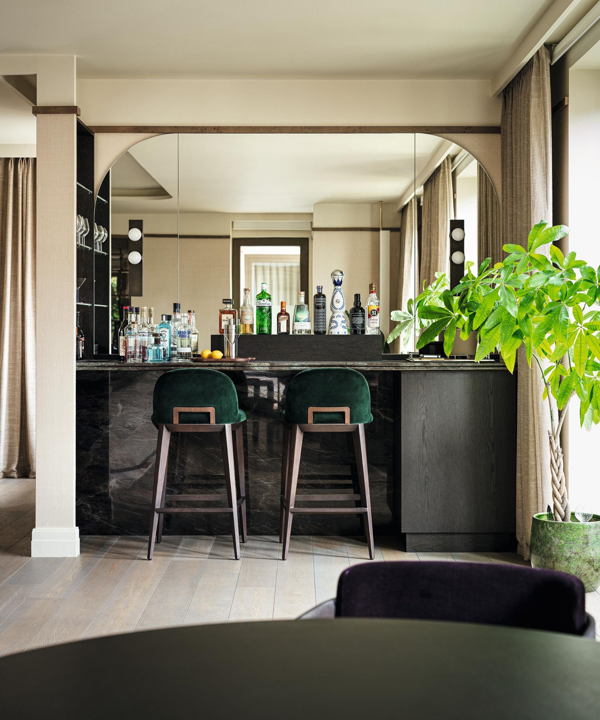 a modern home bar with a dark wooden cabinet area, arched mirror and green bar stools