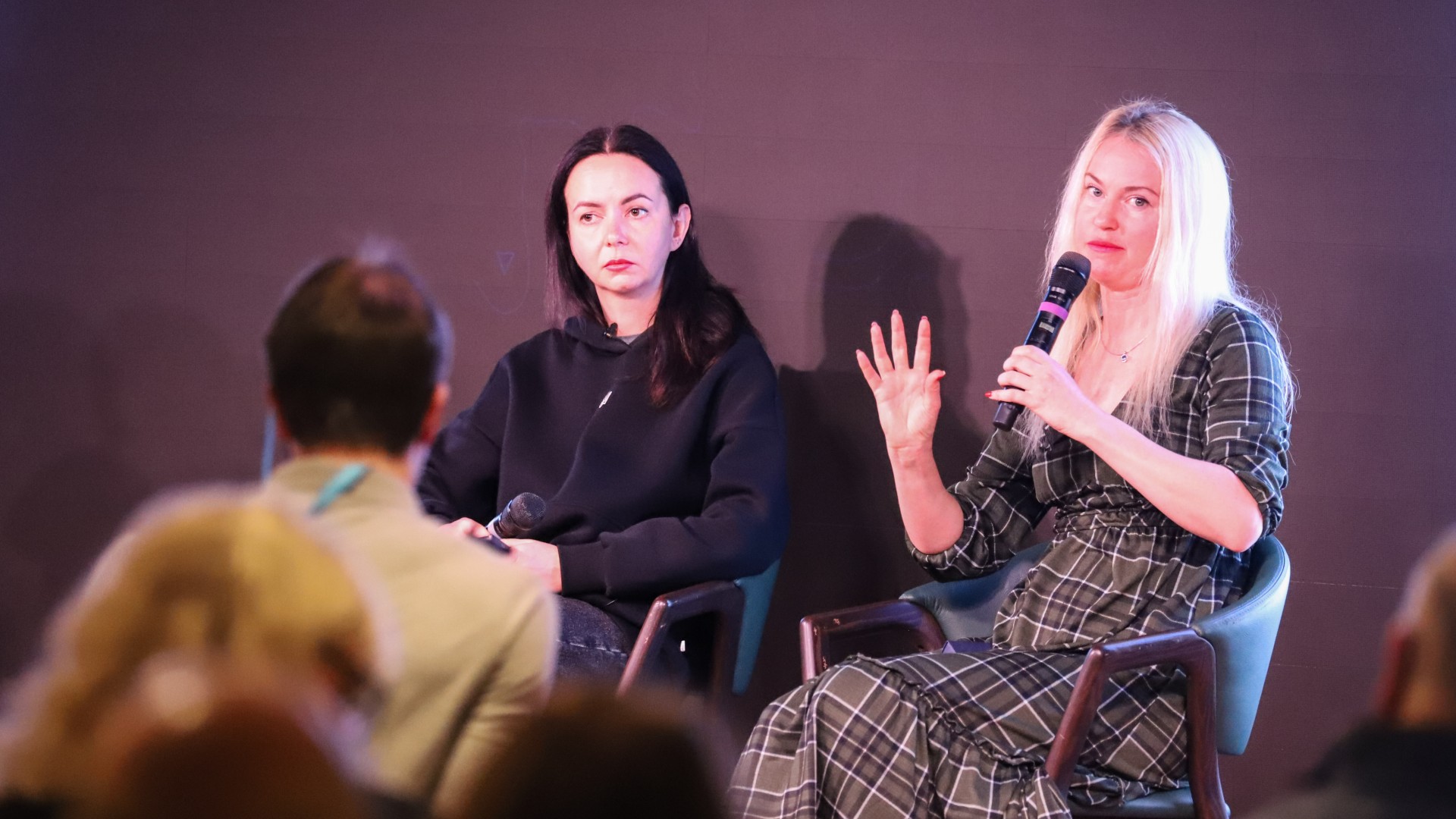 two women speak into microphones in front of a seated crowd