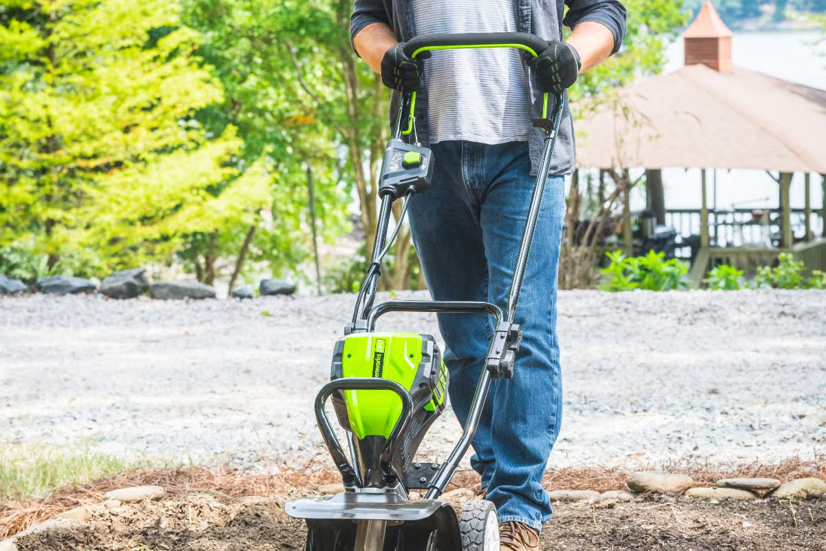 Man pushing GreenWorks tiller in garden bed