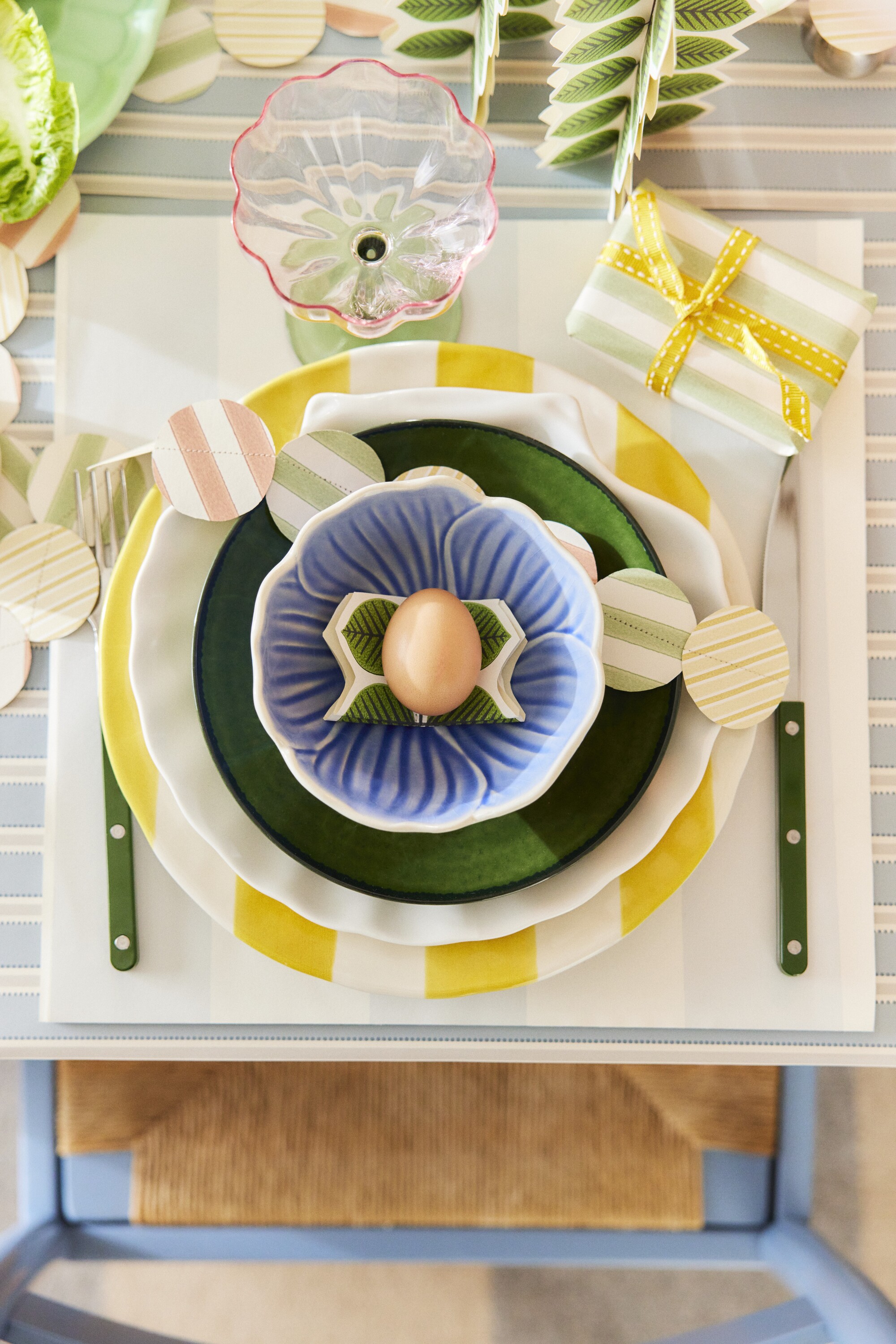 Image of a table place from above with a blue and white striped, wallpaper table cloth with a set of spring plates stacked on each other.
