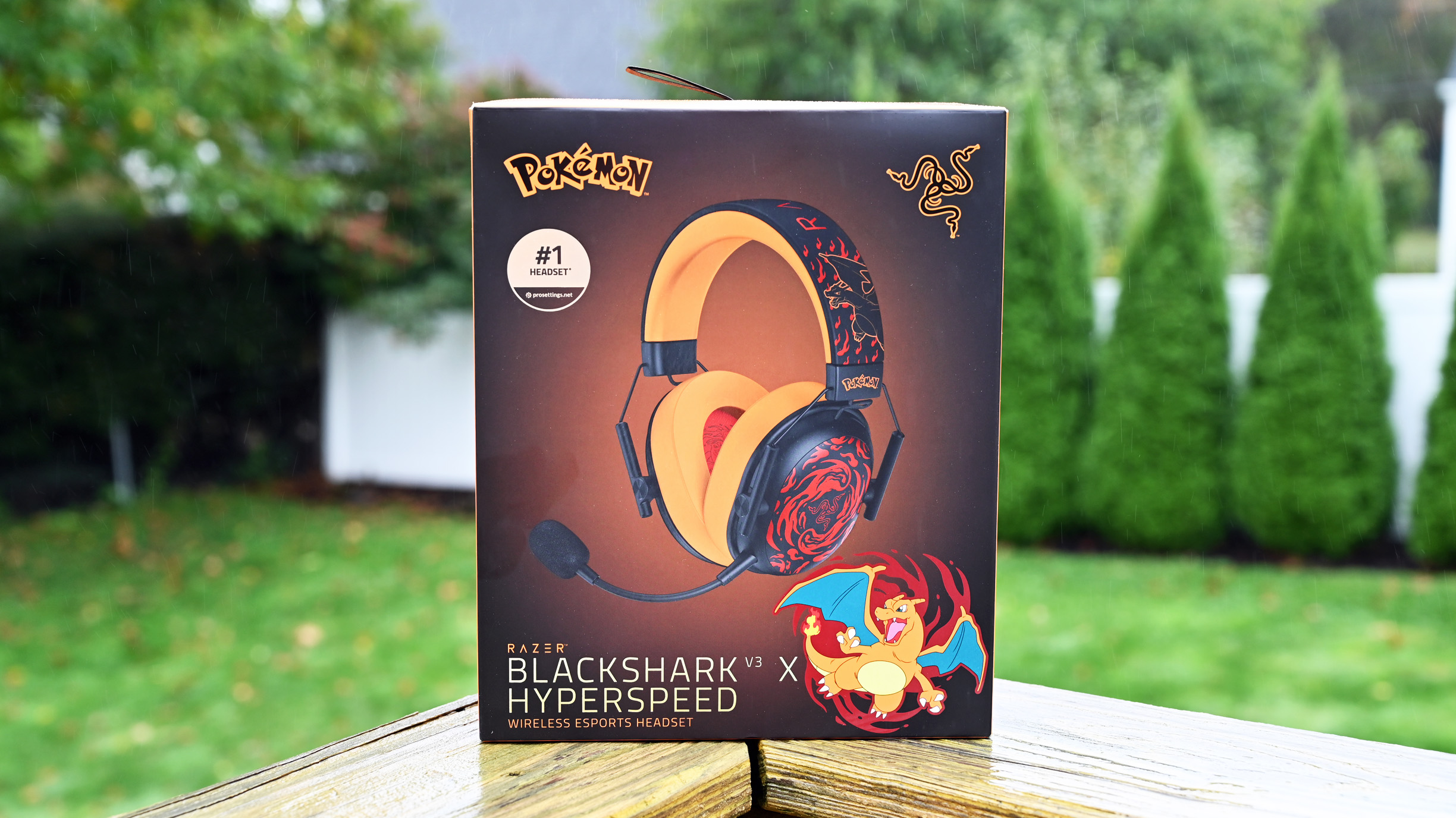 Razer BlackShark V3 X HyperSpeed Charizard Edition retail box on a wood deck with trees in the background.