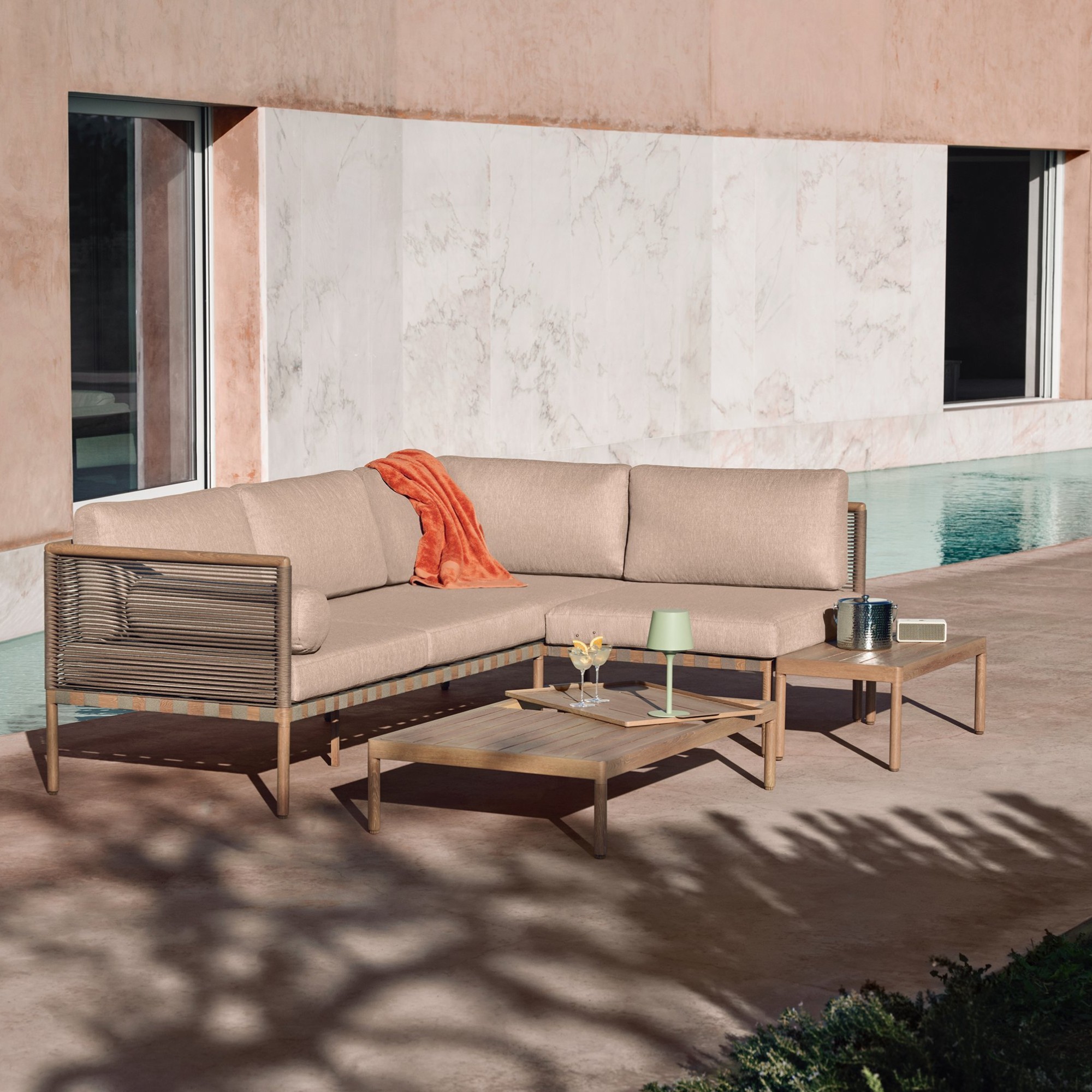 The John Lewis Sahara 5-Seater Modular Corner Garden Lounge Set on a patio of a modern Mediterranean building with a pool