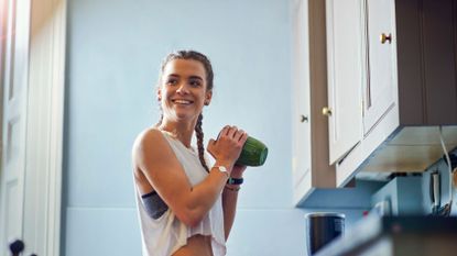 Woman smiling and shaking a green smoothie.