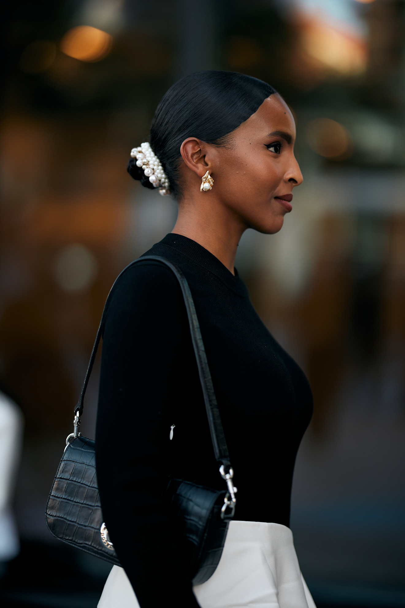 a woman wearing a black sweater and white skirt with a slick back bun and white claw clip