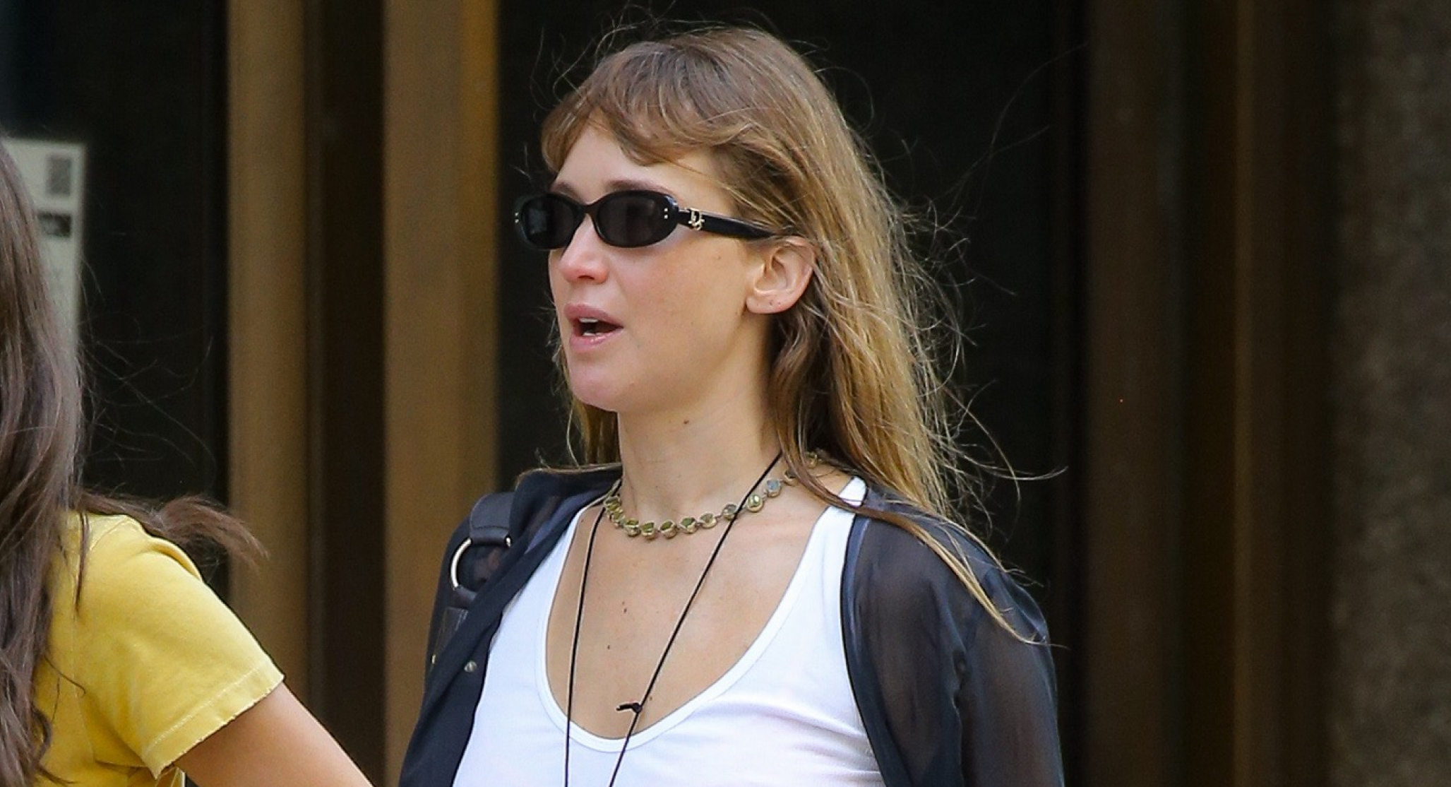 Jennifer Lawrence wearing khaki pants, flip-flops in fall, a white vest and sunglasses