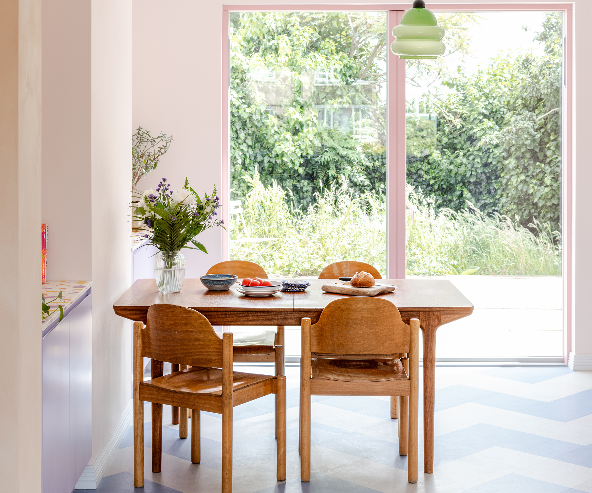 A pastel coloured dining room with pink framed sliding glass doors leading outside
