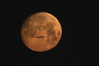 an aircraft's silhouette can be seen in front of the full moon