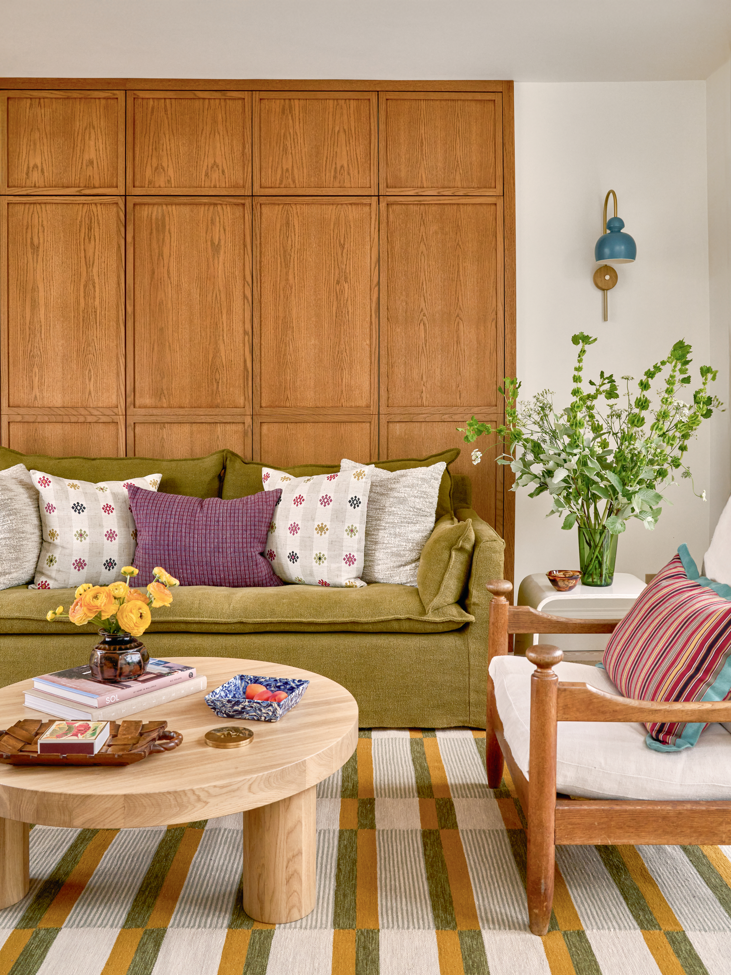 Living area with panelled wall, green sofa, round wood coffee table and green and orange striped rug