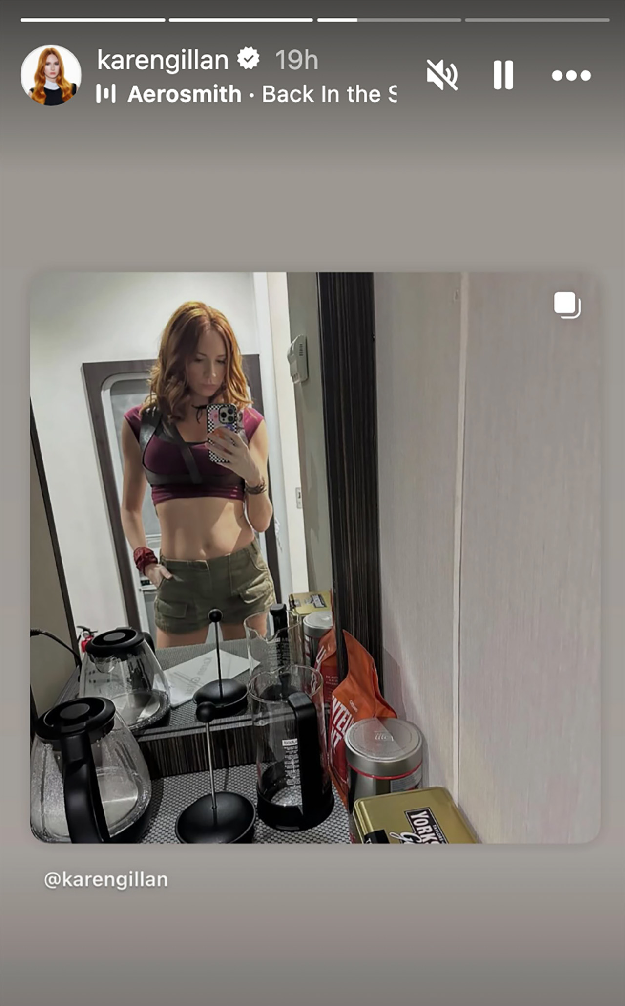 A photo of Karen Gillan taking a selfie in the mirror, she's wearing a crop top and shorts, AKA Ruby Roundhouse's costume.