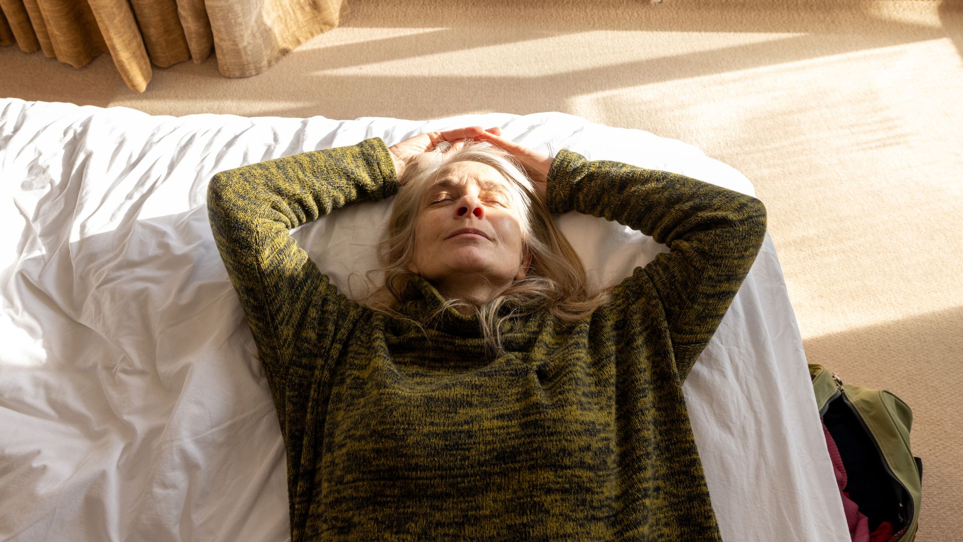 A woman wearing a green sweater lies on her back on a bed.
