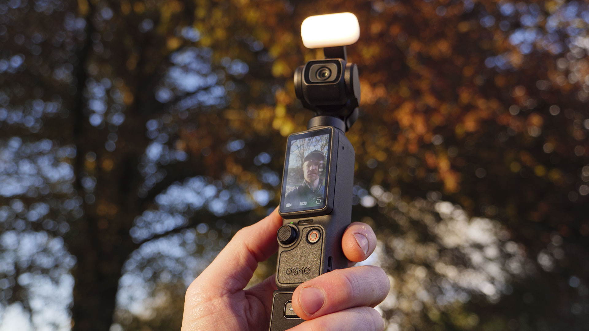 DJI Osmo Pocket 4 vlogging camera with natural background at golden hour, and the user in the frame of the screen