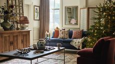 A cozy living room decorated for Christmas, with a large real tree in the right hand corner.