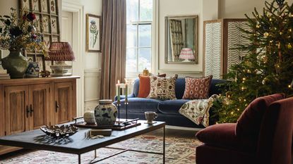 A cozy living room decorated for Christmas, with a large real tree in the right hand corner. 