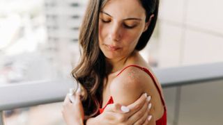 A brunette woman wakes up from her sleep to touch the sunburn on her shoulder