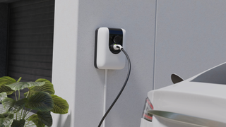 Black and white EV charger on a wall with a car and plant in the shot