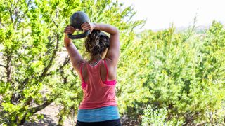 View of woman from behind holding a kettlebell behind her head