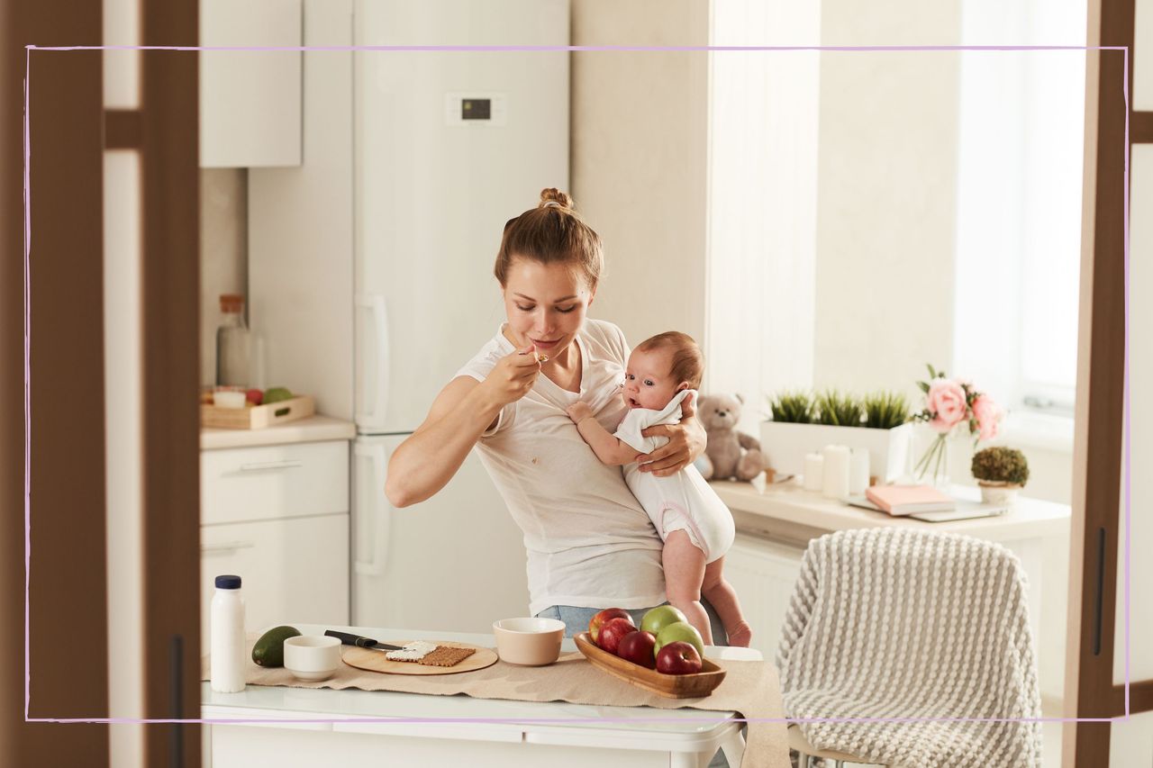 A woman holding a baby and eating while standing up