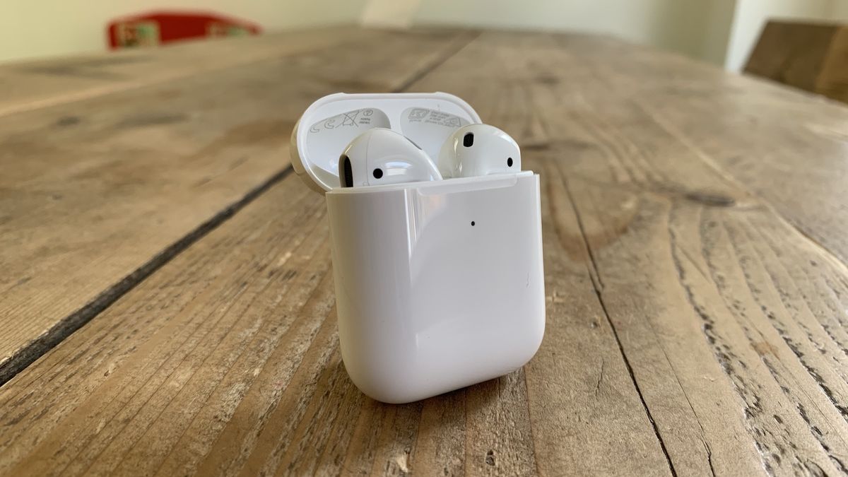 Apple AirPods (2019) in their charging case on a wooden table.