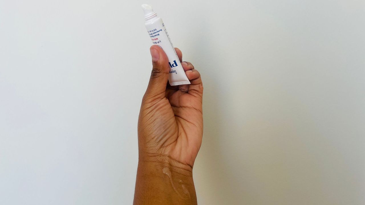 A person holding an opened Supergoop! SPF lip balm.