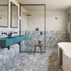 Freestanding bath and seperate shower in grey tiled bathroom with teal sink.